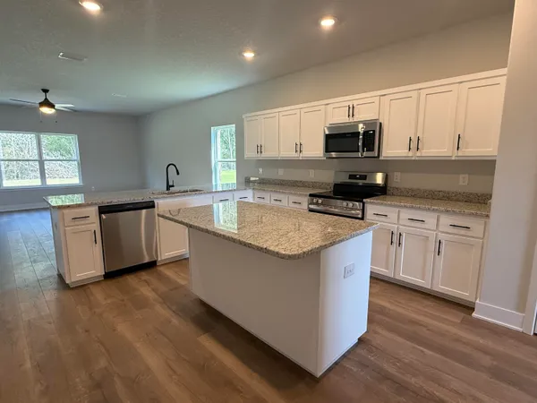 a kitchen with stainless steel appliances a sink a stove a microwave a center island and wooden floor