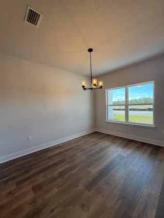 an empty room with wooden floor chandelier and windows