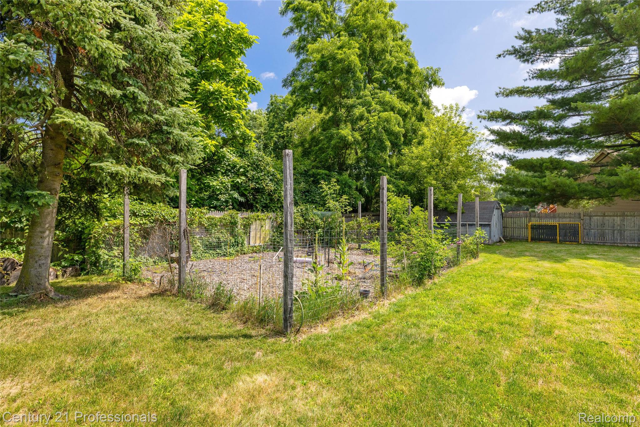 15037 Hogan Road Linden, MI 48451 - Photo 29 of 38 Expansive lawn area featuring a fenced garden space, mature evergreen trees, a wooden privacy fence, and an outdoor storage shed