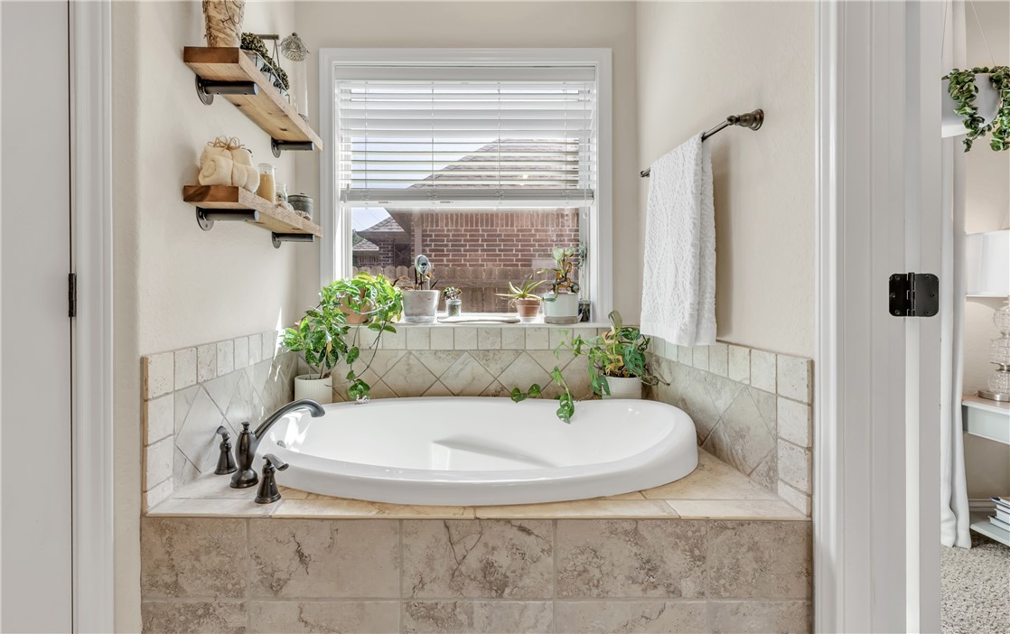8312 Raintree Drive College Station, TX 77845 - Photo 18 of 30 Soaking tub with a tiled surround, bronze-finish faucet, and a window with white blinds
