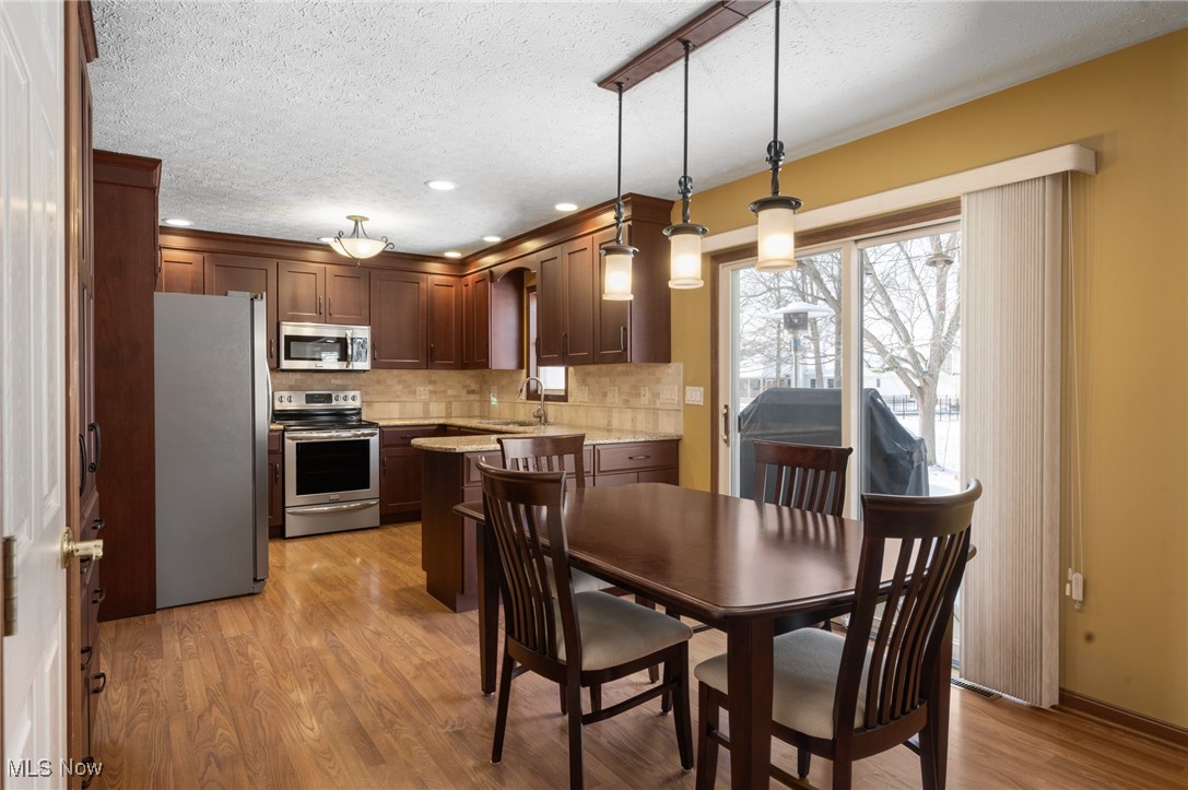 9132 Reed Road North Ridgeville, OH 44039 - Photo 2 of 43 Kitchen with stainless steel appliances, decorative light fixtures, light wood-type flooring, light stone counters, and a textured ceiling