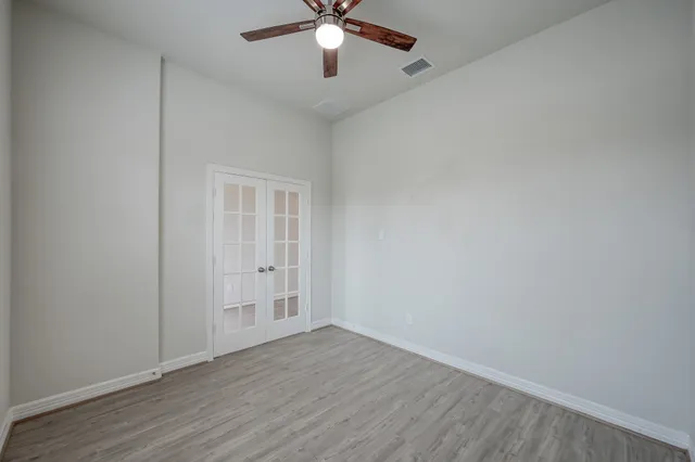 an empty room with wooden floor fan and windows