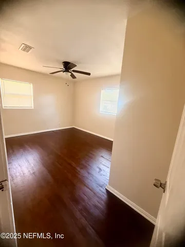 an empty room with wooden floor fan and windows