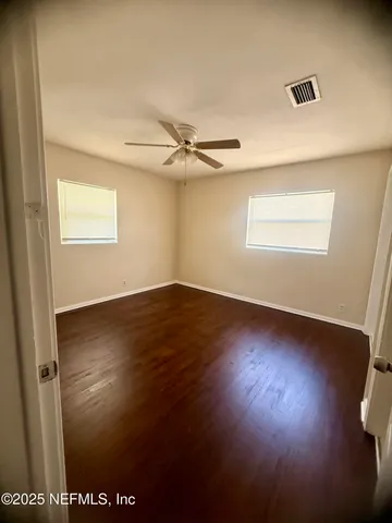 an empty room with wooden floor fan and windows