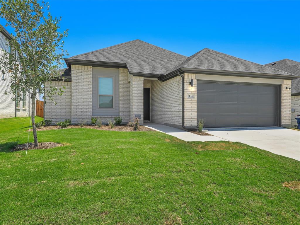 1136 Del Rio Drive Lavon, TX 75166 - Photo 1 of 30 Modern brick residence showcasing a two-car garage with contemporary paneling, professional landscaping with manicured lawn, and clean architectural lines