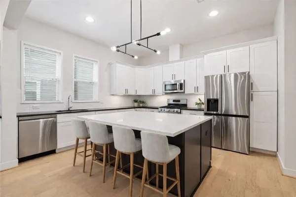 a kitchen with kitchen island a refrigerator a stove a sink and white cabinets with wooden floor