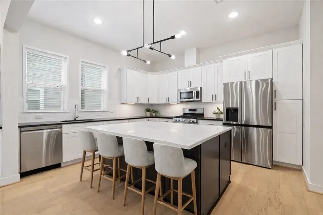 a kitchen with kitchen island a refrigerator a stove a sink and white cabinets with wooden floor