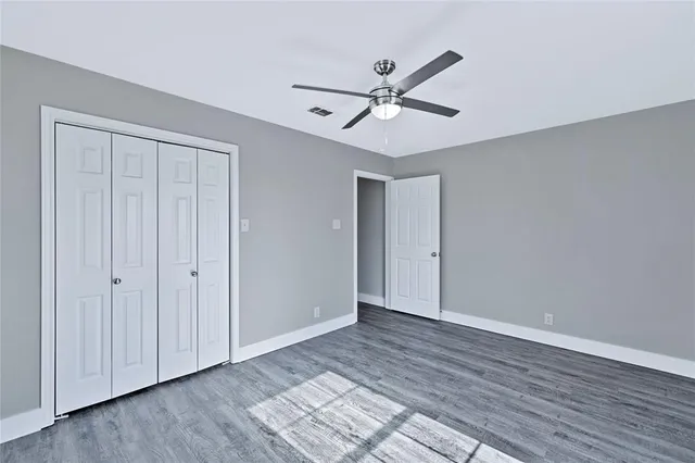 a view of an empty room with wooden floor and a ceiling fan
