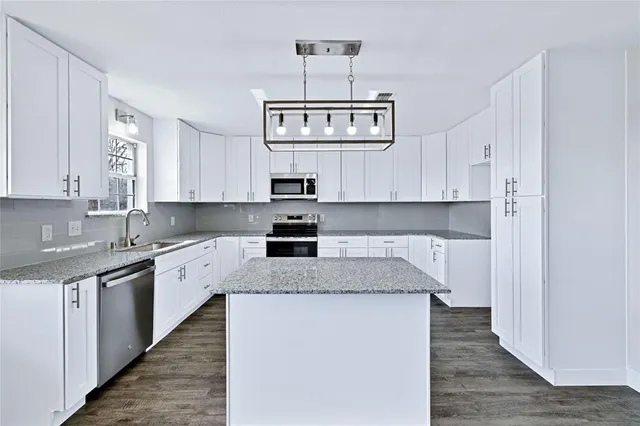 a kitchen with stainless steel appliances granite countertop a sink dishwasher stove and white cabinets with wooden floor