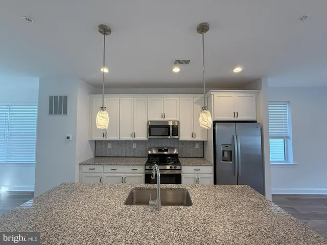 a large kitchen with stainless steel appliances granite countertop a stove a sink a refrigerator and white cabinets with wooden floor