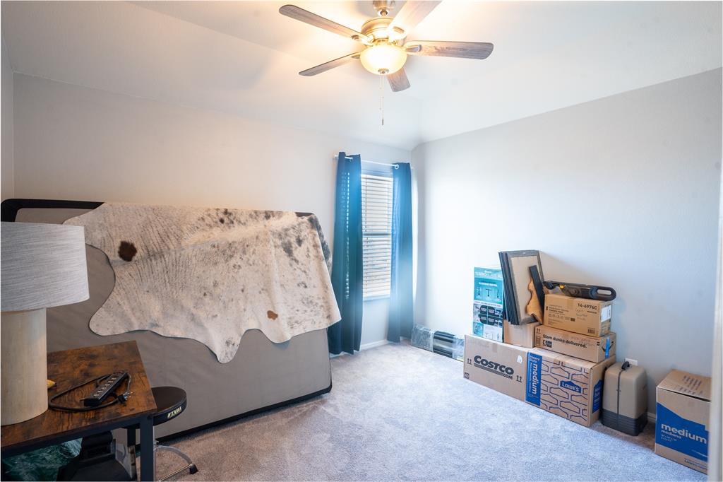 753 Rutherford Drive Crowley, TX 76036 - Photo 22 of 26 Carpeted interior room featuring light gray walls, a ceiling fan with light fixture, and a window with blinds and blue drapes