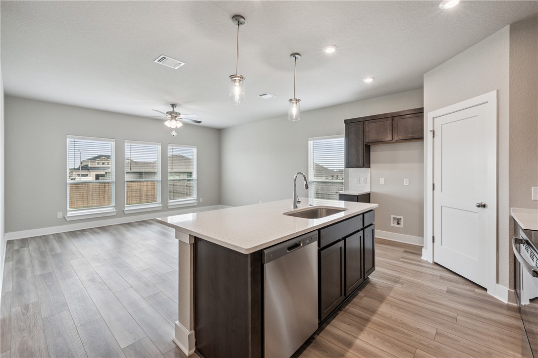 6408 Raleigh Loop College Station, TX 77845 - Photo 5 of 12 Kitchen featuring stainless steel appliances, decorative light fixtures, light stone counters, an island with sink, and light wood-type flooring