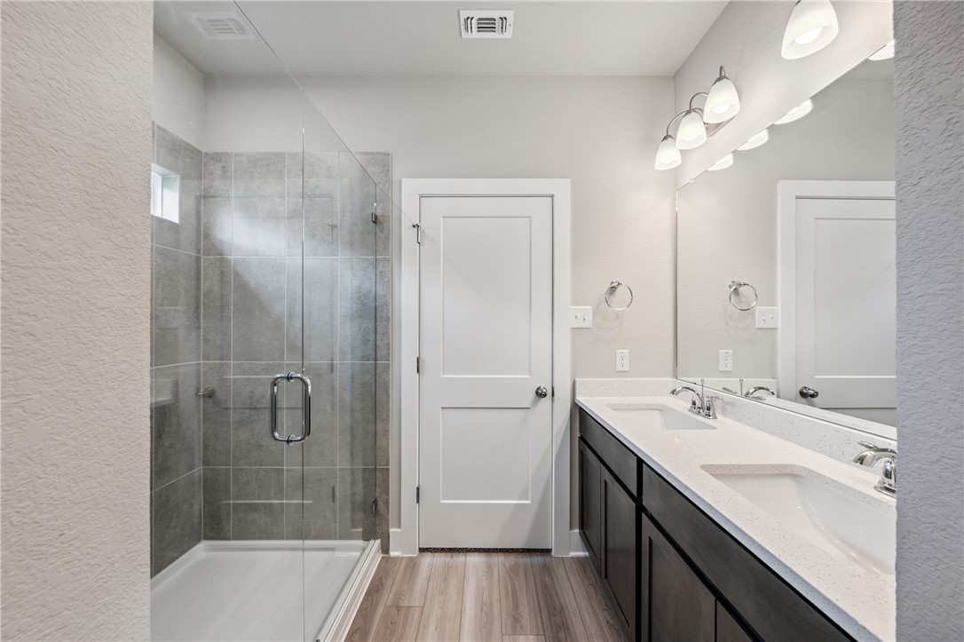 6408 Raleigh Loop College Station, TX 77845 - Photo 7 of 12 Bathroom with double vanity, a shower stall, light wood finished floors, and a textured wall