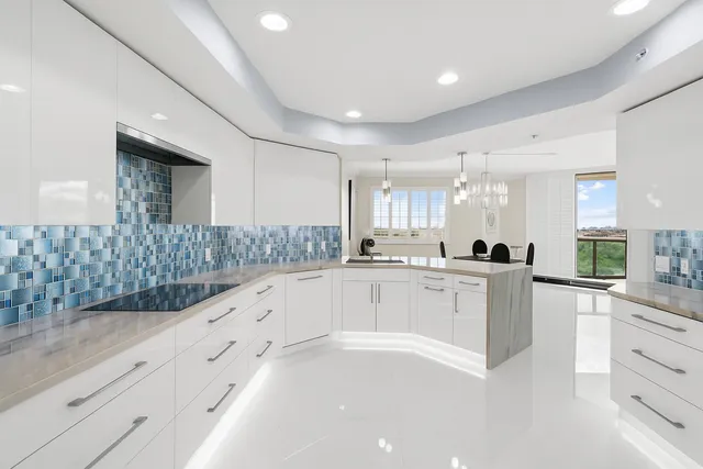 a large white kitchen with granite countertop a stove a sink a refrigerator and white cabinets with wooden floor