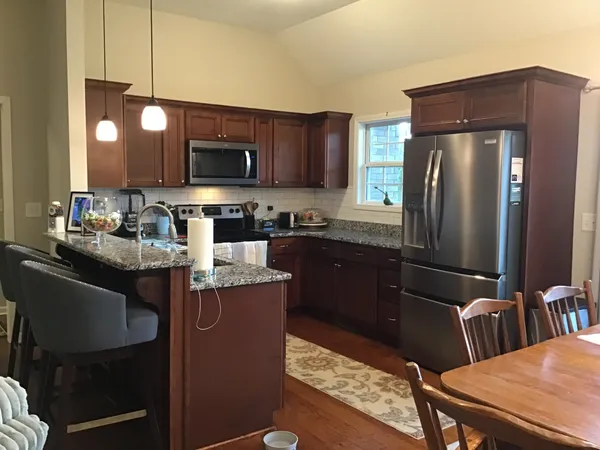 a kitchen with stainless steel appliances granite countertop a refrigerator a stove a sink a dining table and chairs