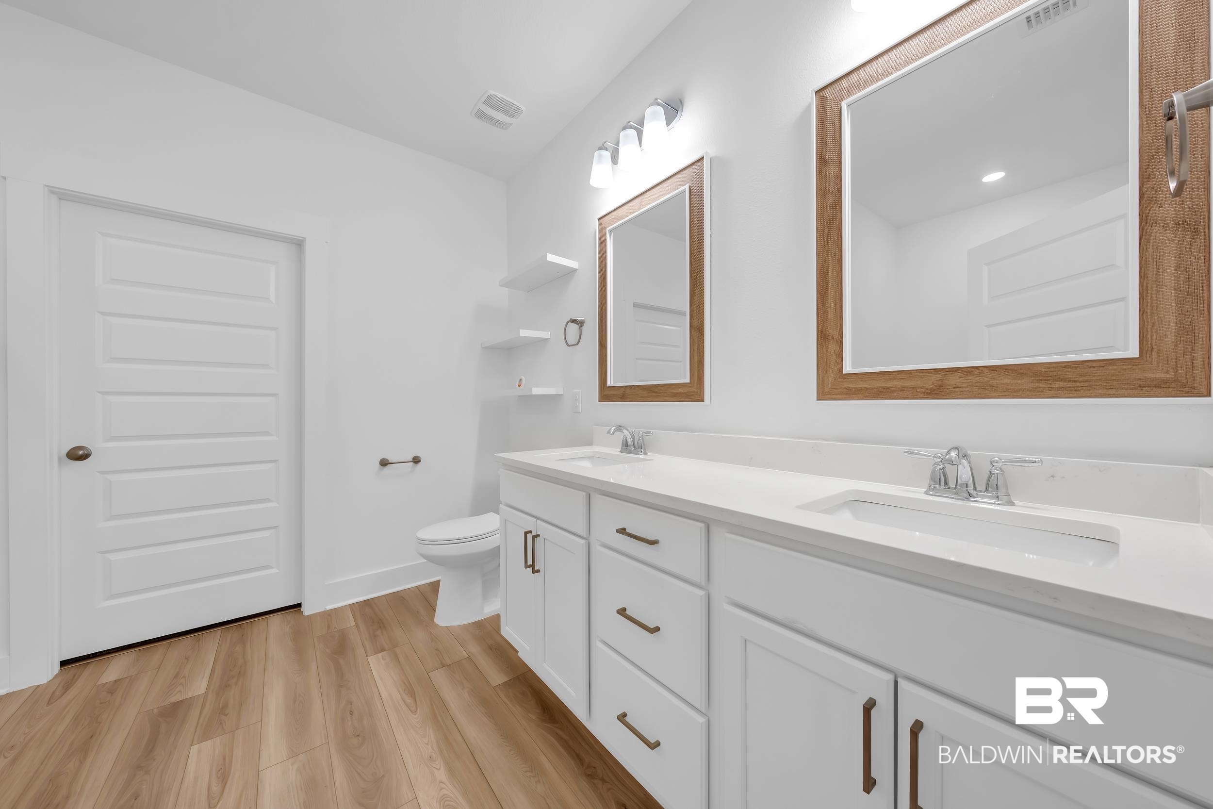 9933 Weller Cove Foley, AL 36535 - Photo 18 of 36 Dual vanity with white cabinetry, wood-finish flooring, white countertops, two framed mirrors, and chrome fixtures