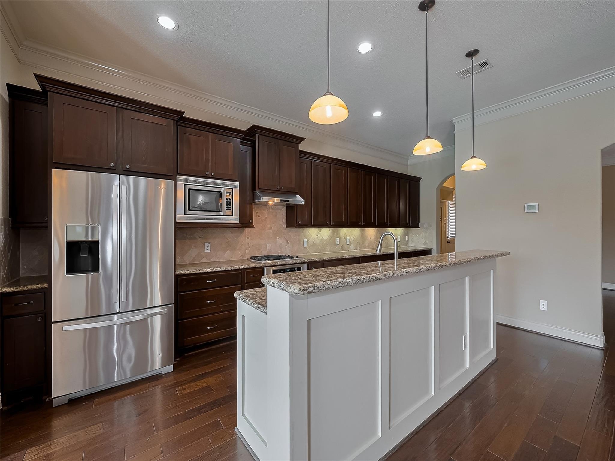 2711 King Point View Lane Spring, TX 77388 - Photo 9 of 48 This modern kitchen features stainless steel appliances, dark wood cabinetry, granite countertops, and an elegant tile backsplash. A spacious island with pendant lighting provides additional workspace and seating.
