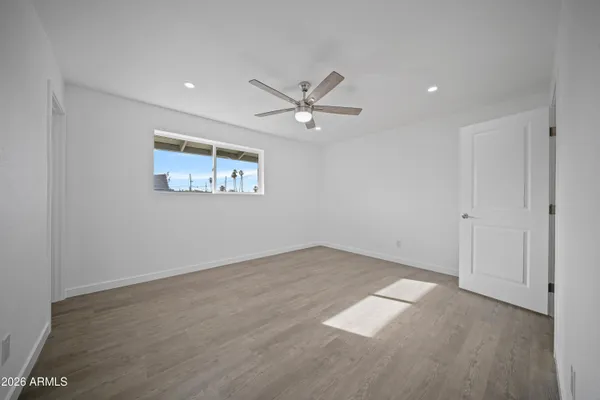 a view of an empty room with wooden floor and a ceiling fan