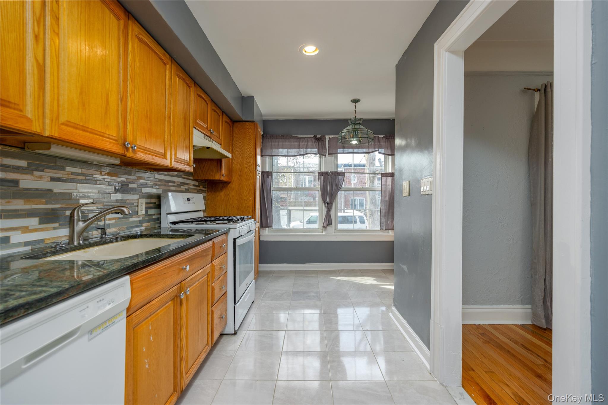 179-65 Selover Road Queens, NY 11434 - Photo 12 of 33 Galley kitchen 9'5" x 14'11"Kitchen featuring wood cabinetry, a mosaic tile backsplash, dark countertops, white appliances, and light-colored tile flooring