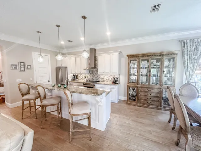 a kitchen with stainless steel appliances kitchen island granite countertop a stove a refrigerator a dining table and chairs with wooden floor