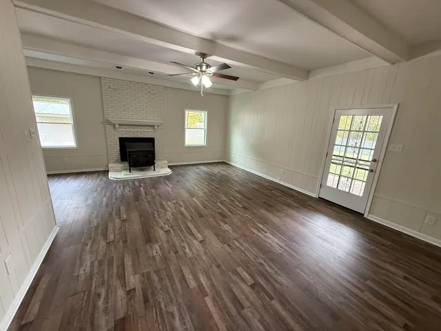 an empty room with wooden floor fireplace and windows