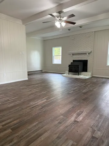a view of an empty room with wooden floor fireplace and a window