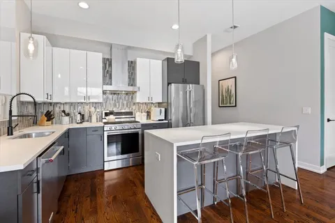 a kitchen with stainless steel appliances a stove a sink dishwasher a refrigerator white cabinets and wooden floor next to a window