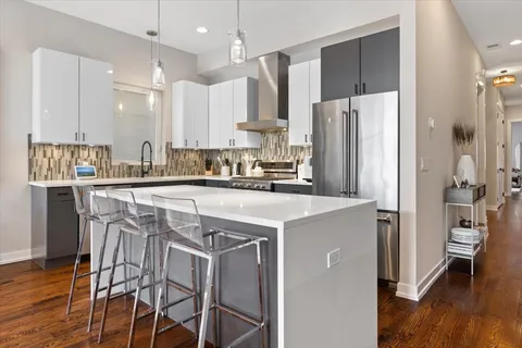 a kitchen with stainless steel appliances a refrigerator a sink a stove and white cabinets with wooden floor