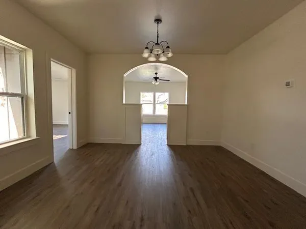 an empty room with wooden floor chandelier and windows