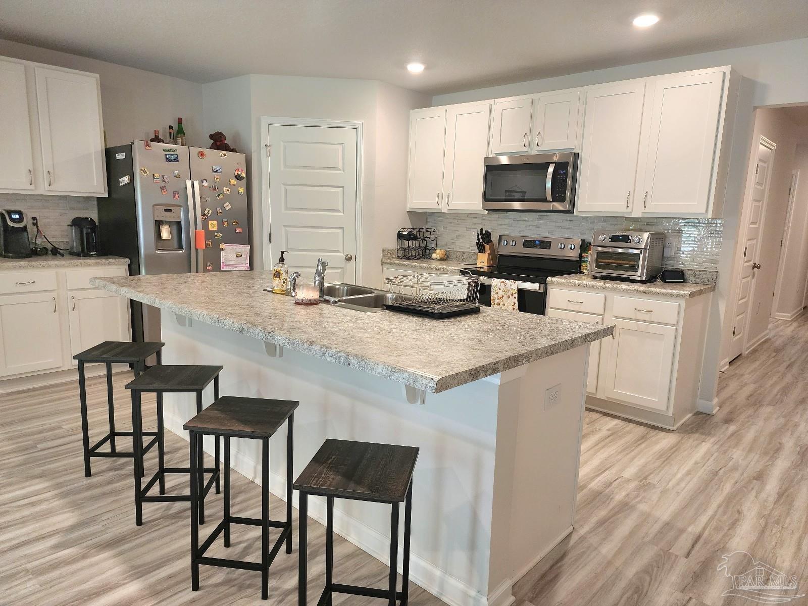 5379 Peach Drive Pace, FL 32571 - Photo 5 of 23 a kitchen with stainless steel appliances granite countertop a stove a sink a microwave a refrigerator a dining table and chairs with wooden floor