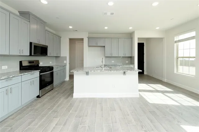 a large white kitchen with kitchen island a sink a counter space and stainless steel appliances