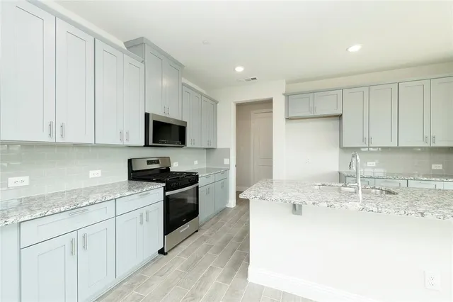 a kitchen with stainless steel appliances granite countertop a sink a stove top oven a refrigerator with white cabinets and a granite counter tops