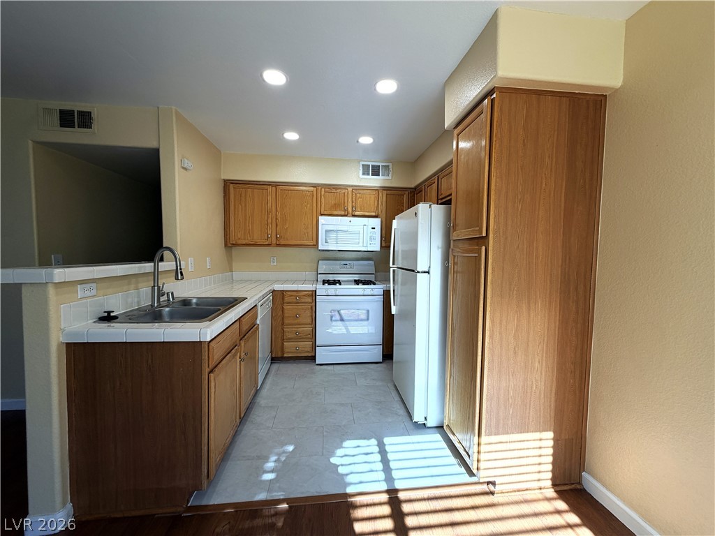 4955 South Lindell Road, Unit 203 Las Vegas, NV 89118 - Photo 5 of 31 A functional kitchen features wood cabinetry and white appliances, with ample counter space for culinary tasks.