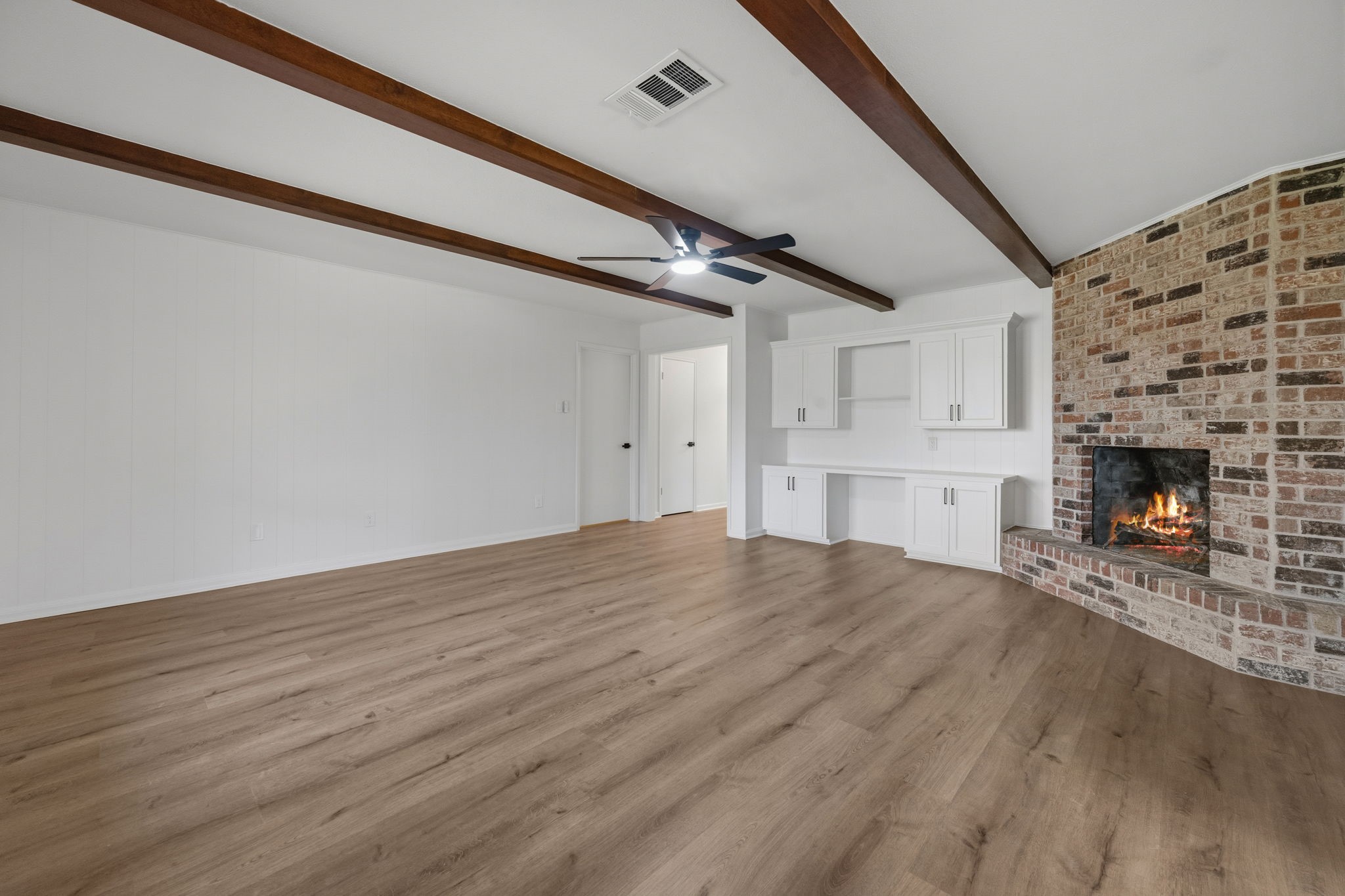 210 Ridgemont Drive Alvin, TX 77511 - Photo 12 of 27 This spacious living room features a cozy brick fireplace, wooden ceiling beams, light wood floors, and built-in white cabinetry, creating a warm and inviting atmosphere.