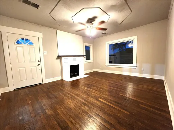 a view of an empty room with wooden floor fireplace and a window