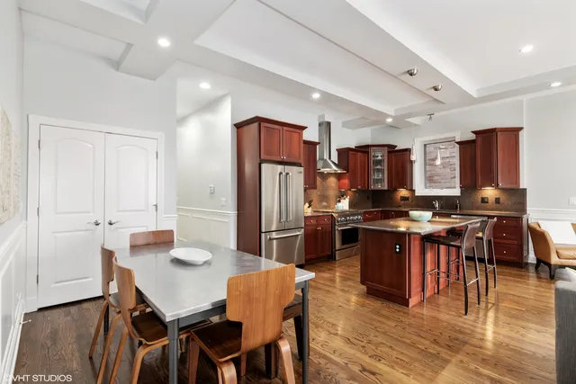 a kitchen with stainless steel appliances kitchen island granite countertop a dining table chairs and refrigerator
