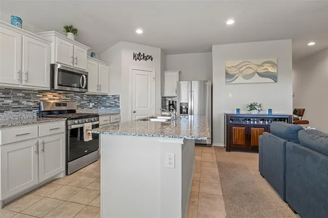 a kitchen with stainless steel appliances granite countertop a stove top oven a sink a refrigerator and white cabinets