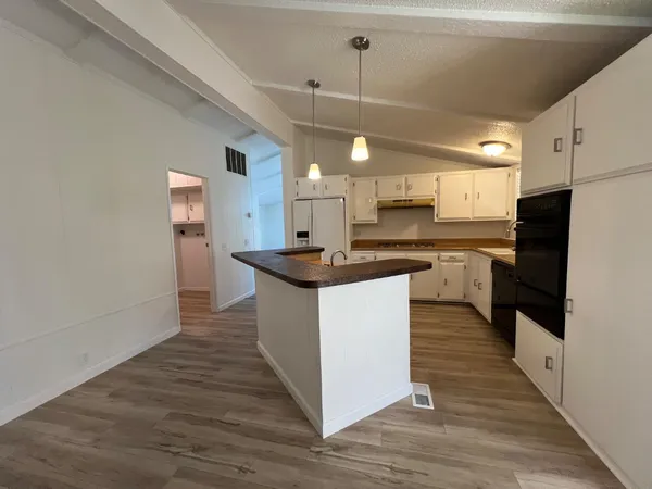 a kitchen with stainless steel appliances granite countertop a refrigerator a sink dishwasher a stove and white cabinets with wooden floor