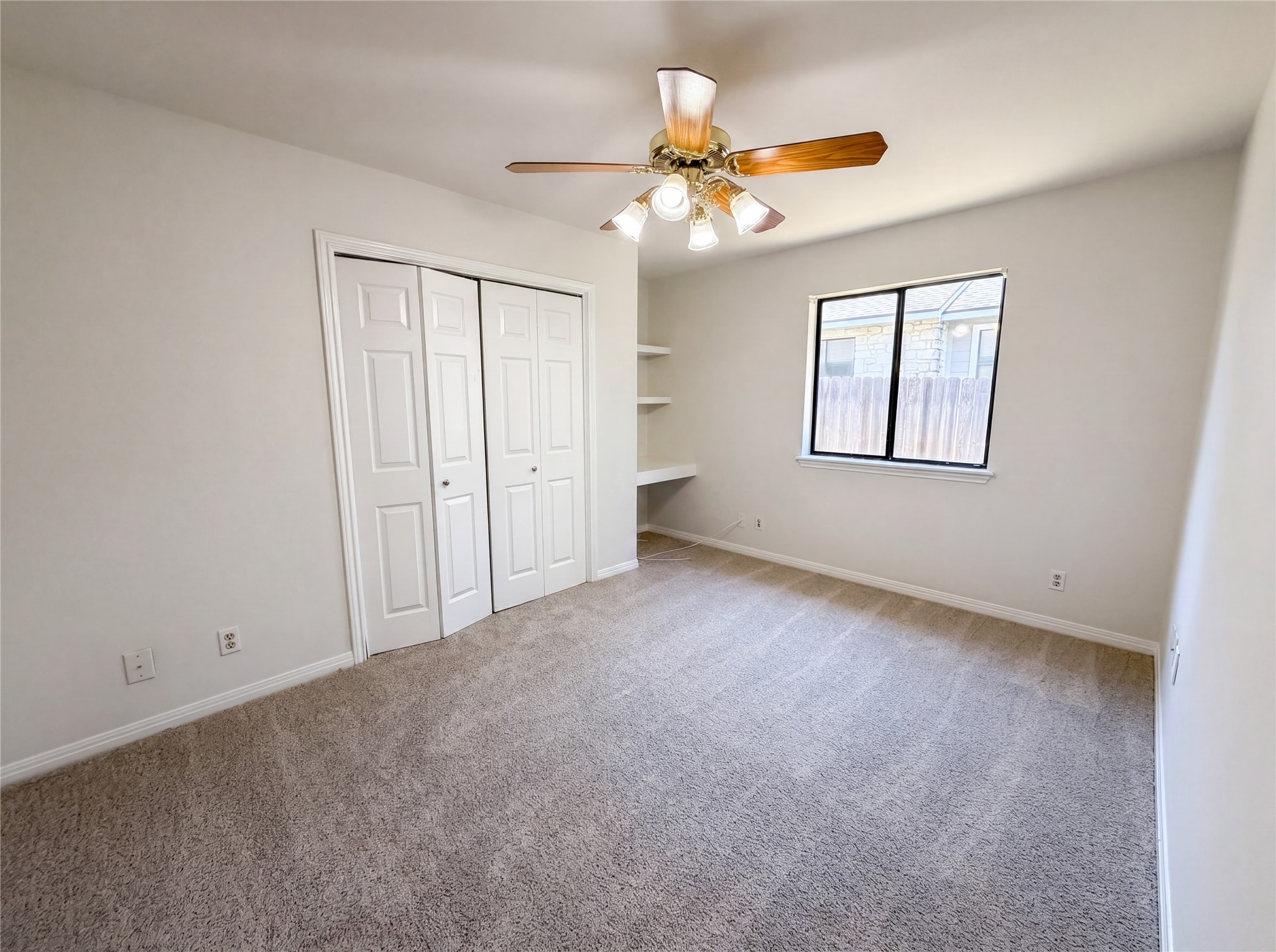 1111 North Riviera Circle Cedar Park, TX 78613 - Photo 4 of 17 Neutral-toned room featuring wall-to-wall carpeting, a multi-pane window, built-in shelving, a ceiling fan with integrated lighting, and bifold closet doors