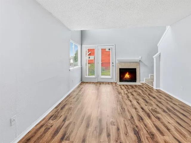 a view of an empty room with wooden floor fireplace and a window
