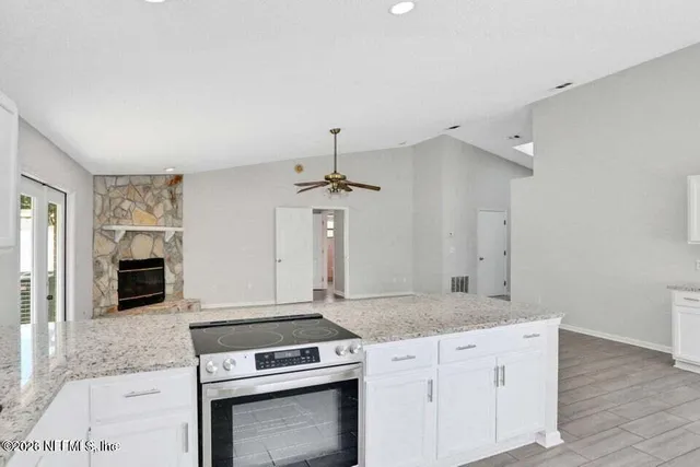 a kitchen with granite countertop a stove and white cabinets with wooden floor