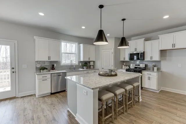 a kitchen with stainless steel appliances granite countertop a stove a sink a microwave oven a refrigerator and white cabinets with wooden floor