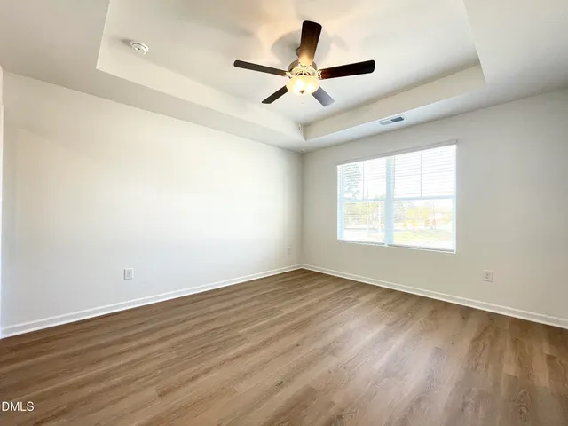 an empty room with wooden floor ceiling fan and windows