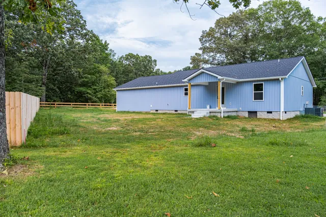 a house that is sitting in the grass with large trees and plants