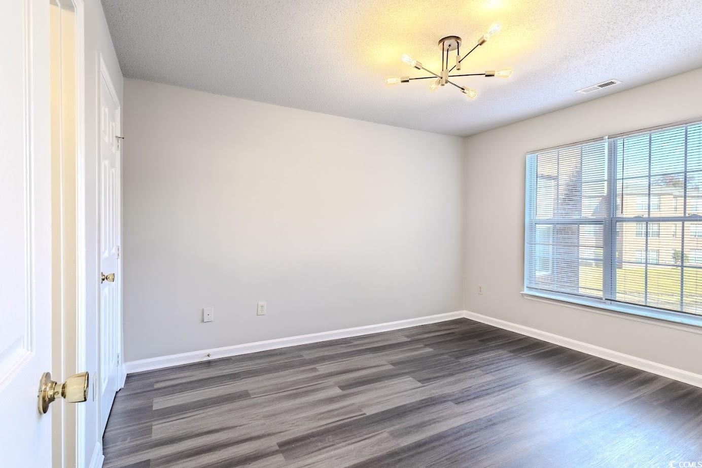 4246 Villas Drive, Unit 706 Little River, SC 29566 - Photo 13 of 20 Spare room featuring dark wood-type flooring, a chandelier, and a textured ceiling