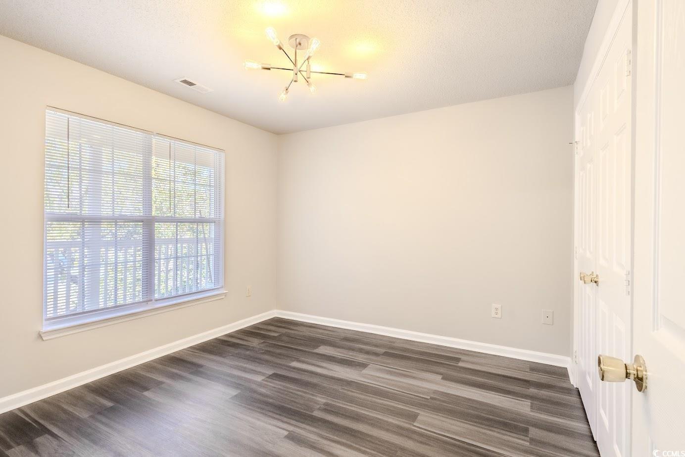 4246 Villas Drive, Unit 706 Little River, SC 29566 - Photo 17 of 20 Spare room featuring dark wood-type flooring, a chandelier, and a textured ceiling