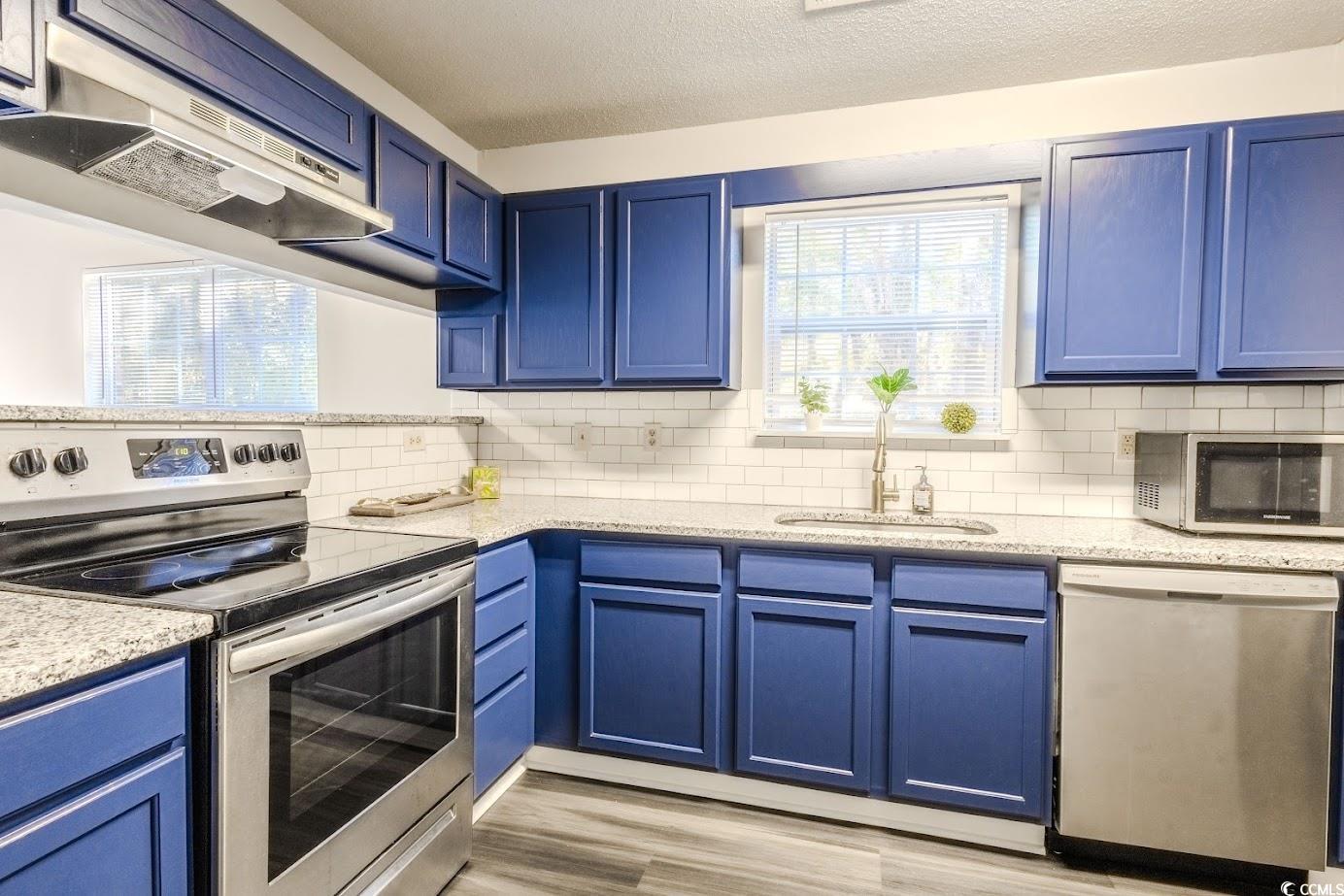 4246 Villas Drive, Unit 706 Little River, SC 29566 - Photo 6 of 20 Kitchen featuring blue cabinetry, appliances with stainless steel finishes, ventilation hood, light stone countertops, and a textured ceiling