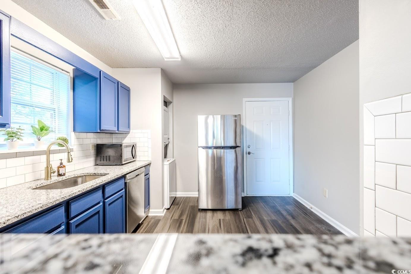 4246 Villas Drive, Unit 706 Little River, SC 29566 - Photo 7 of 20 Kitchen with blue cabinets, light stone countertops, appliances with stainless steel finishes, dark wood-type flooring, and a textured ceiling
