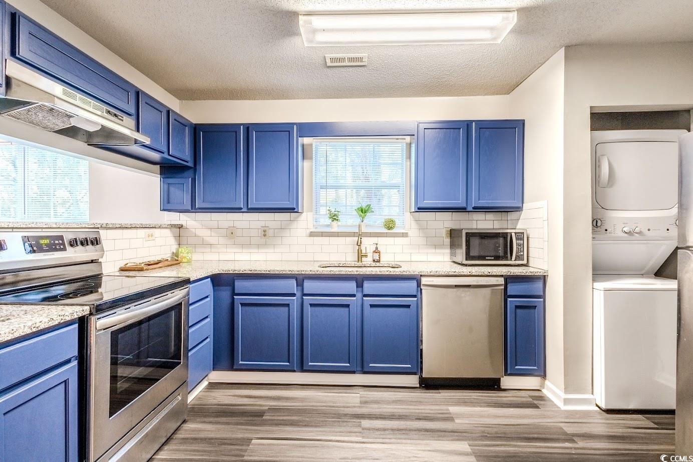 4246 Villas Drive, Unit 706 Little River, SC 29566 - Photo 8 of 20 Kitchen with blue cabinets, appliances with stainless steel finishes, stacked washer / dryer, and a textured ceiling