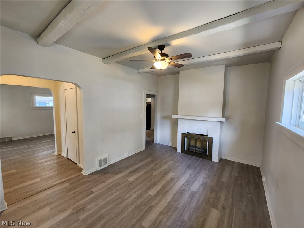 7202 Snow Road Parma, OH 44129 - Photo 3 of 14 Unfurnished living room featuring beamed ceiling, a fireplace, ceiling fan, and hardwood / wood-style flooring